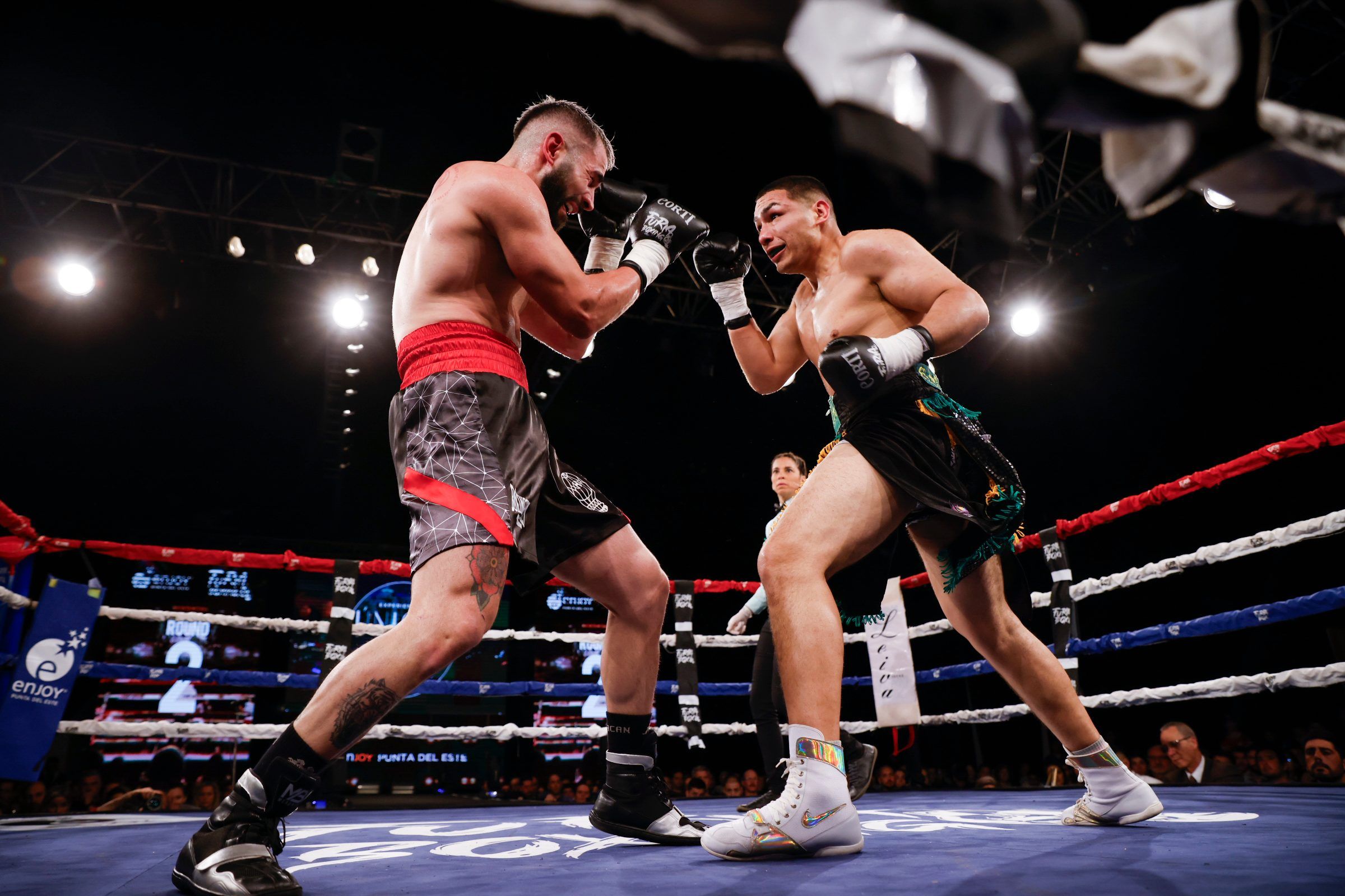 Dos boxeadores intercambian golpes en el ring de la velada de Furia Boxing, con la marca de Enjoy Punta del Este en las cuerdas