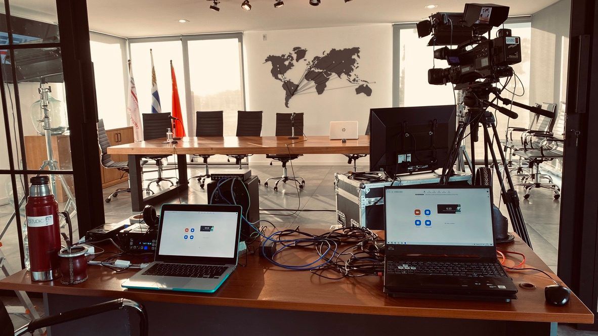 Cámara de transmisión sobre trípode, notebooks y equipos de conexión armados sobre la mesa de la sala de una auditoría virtual