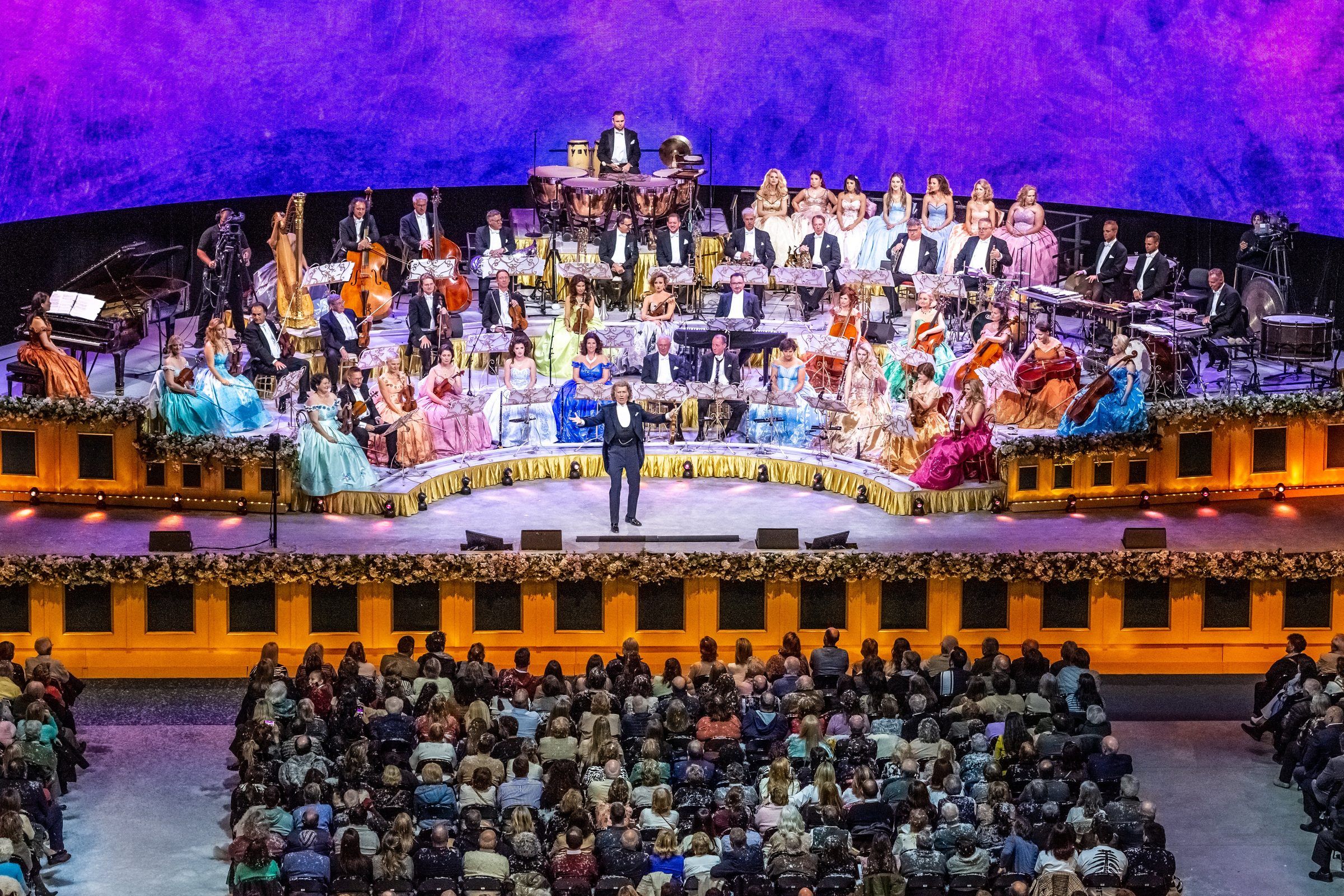 André Rieu frente a la orquesta en el escenario del Antel Arena, con camarógrafos a los costados y la platea adelante