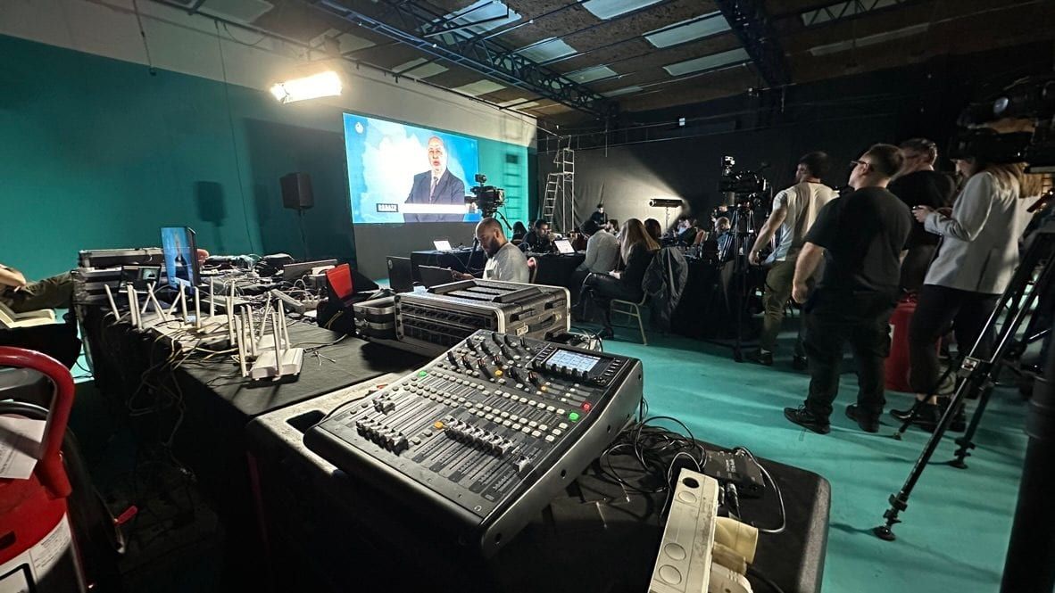 Mezclador de audio y puesto técnico frente a la pantalla del debate, con el equipo de producción al fondo.