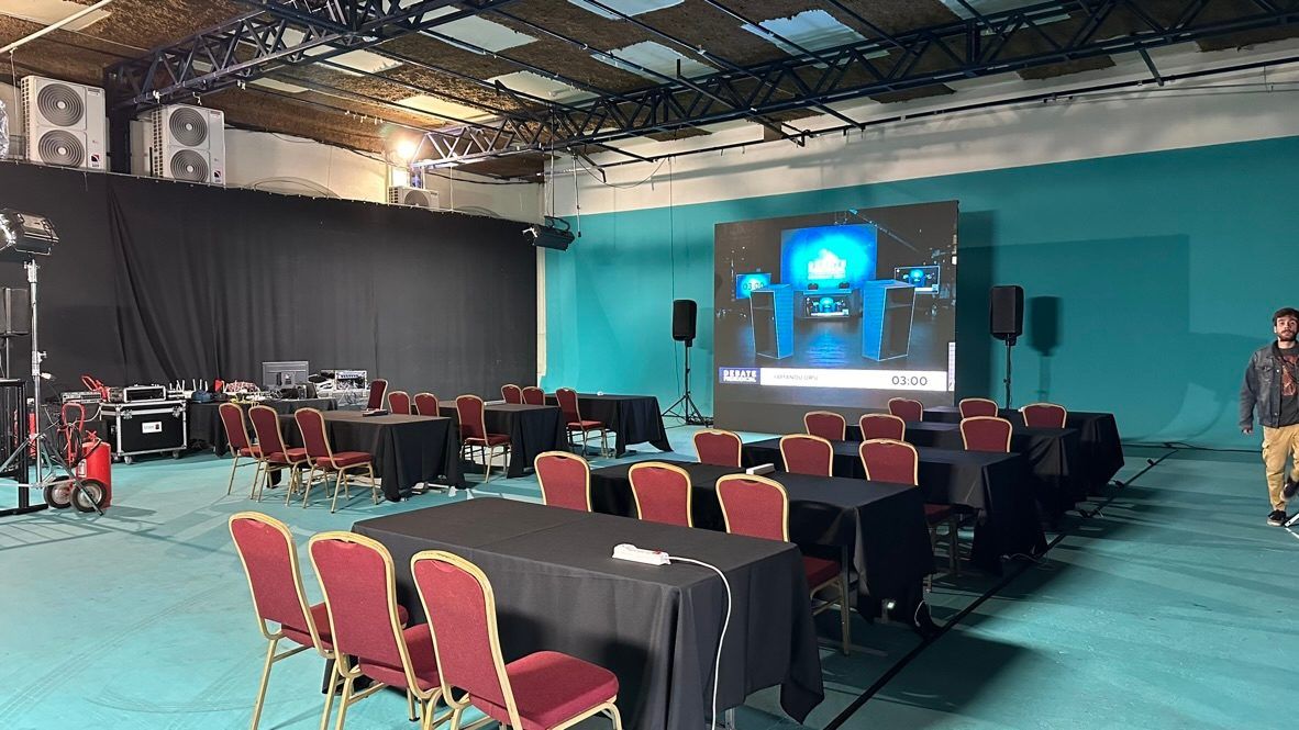 Set del debate antes del evento: pantalla con el logo del debate, mesas y sillas del sector de prensa y equipos de control sobre el lateral