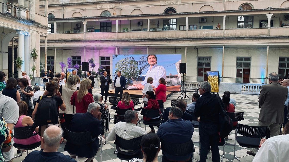 Asistentes frente a la pantalla del escenario durante la presentación, con una cámara a la derecha.