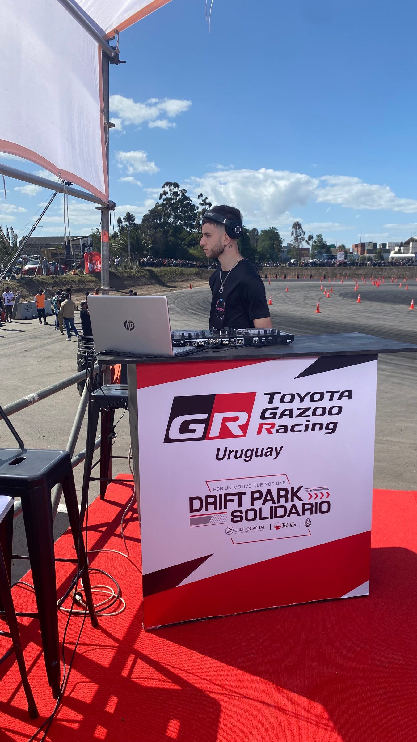 Presentador con una notebook detrás de la mesa de la marca Toyota Gazoo Racing Uruguay, con la gráfica del Drift Park Solidario, sobre la alfombra roja del set