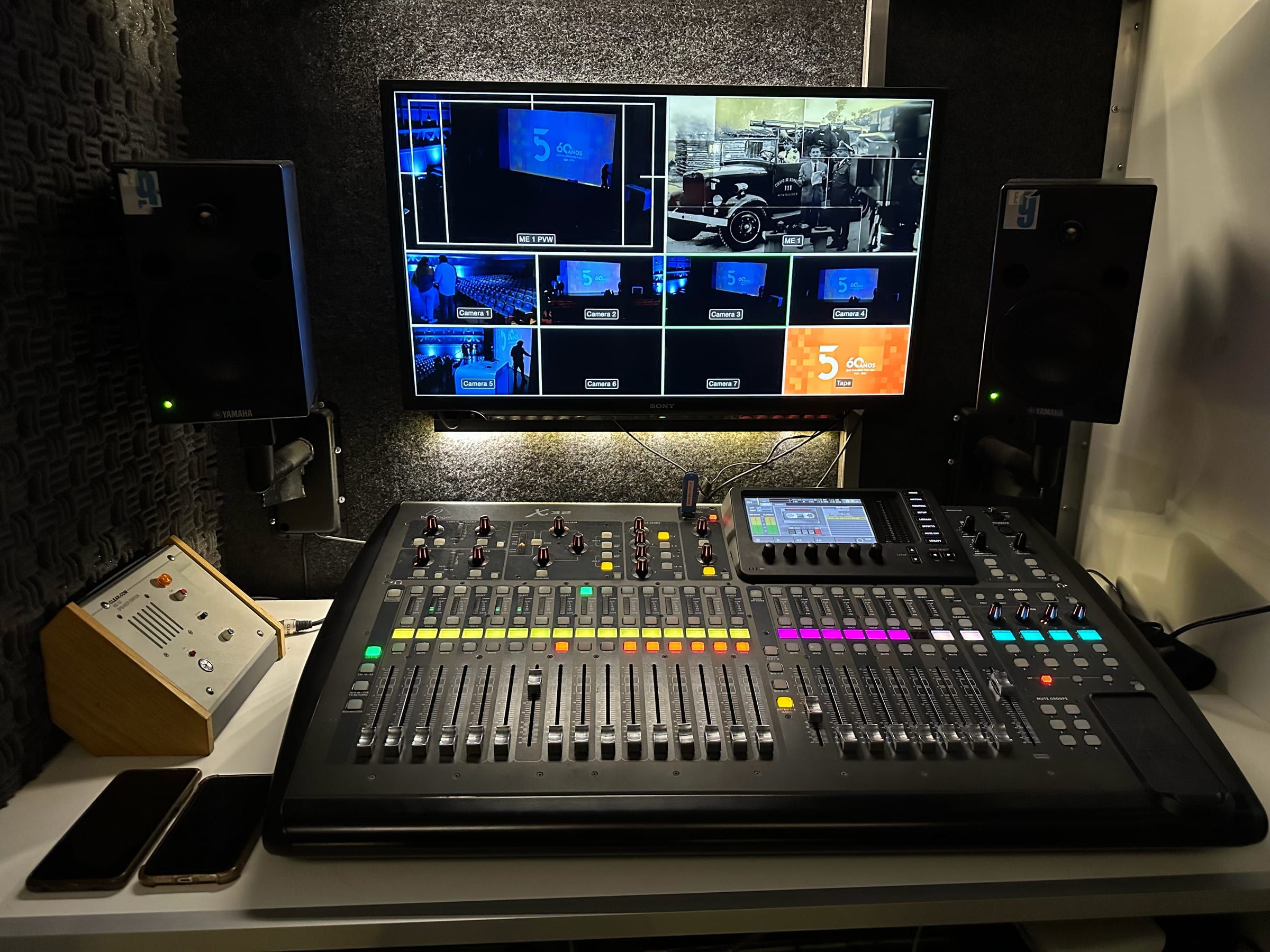 Cabina de audio del camión: consola digital frente a un monitor con las cámaras de la transmisión y dos parlantes de estudio
