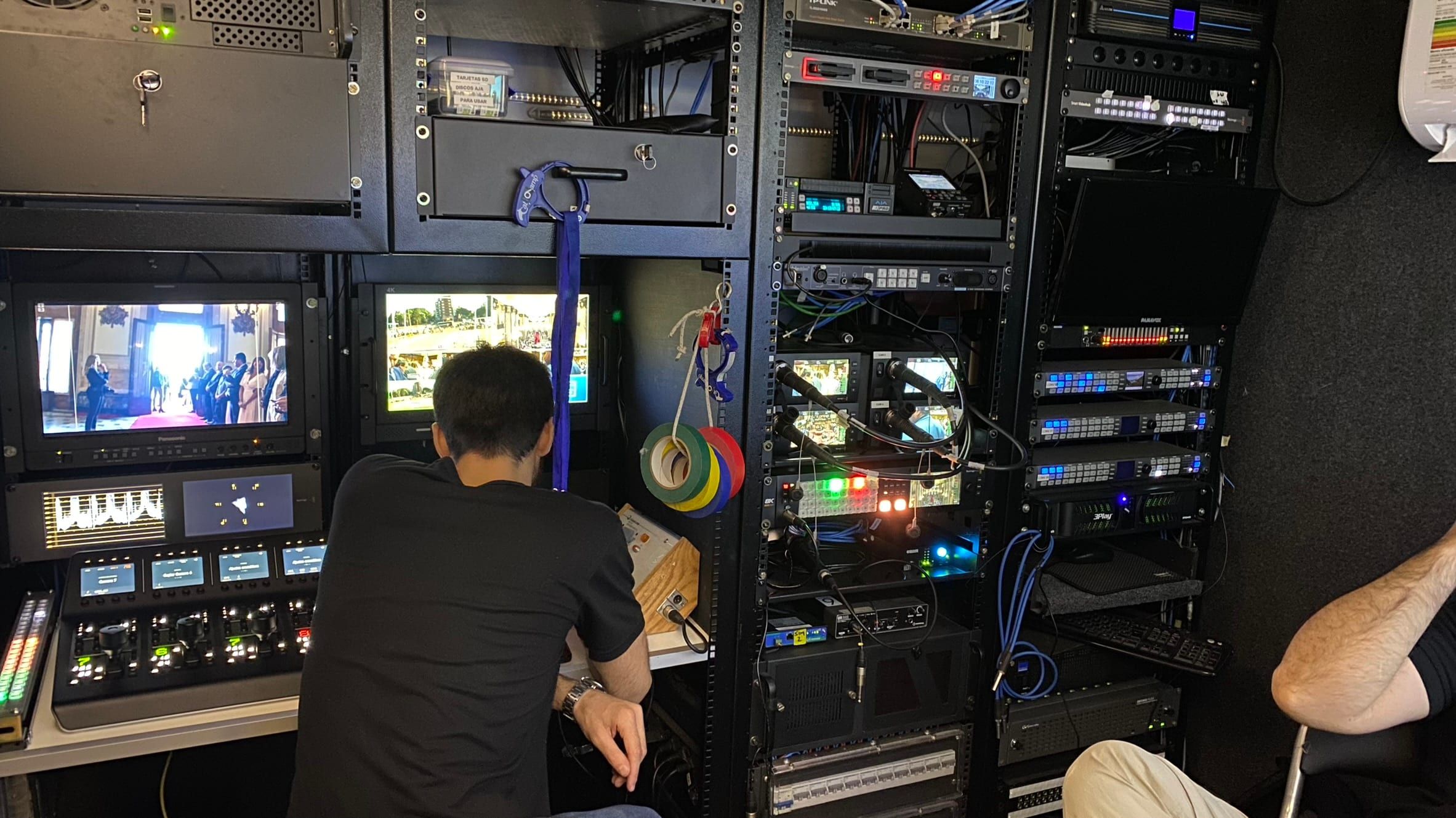 Técnico de video frente al rack del camión, con monitores de ajuste, paneles de control de cámaras y equipos de video
